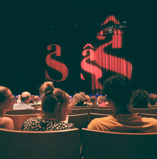 Personnes assises dans une salle de spectacle, avec le rideau baissé